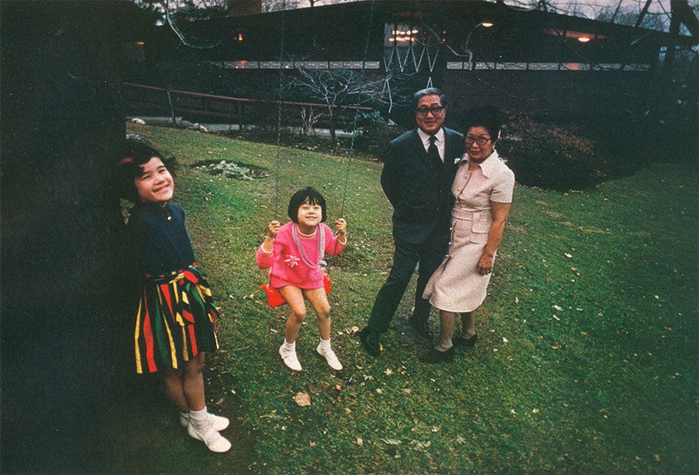 Family of 4 poses for a picture on a grassy field in front of their house