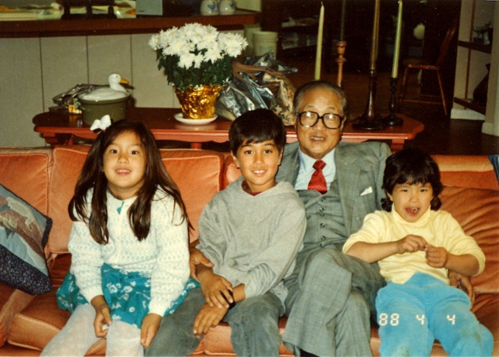 Sugahara sits on a couch with 3 grandchildren